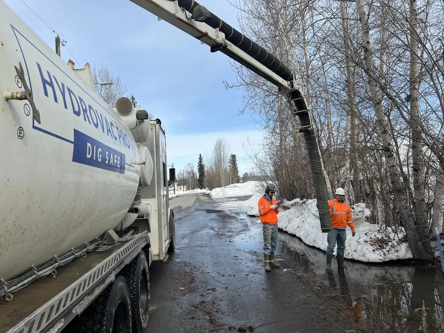 Hydrovac Pro crew operating the vacuum boom beside the Dig Safe truck on an Alaska job site